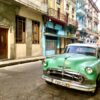 Grüner Oldtimer vor einer farbenfrohen Häuserkulisse im Centro Havannas auf Kuba - Gruppenreisen für Alleinreisende & Erlebnisreisen | QUERIDO MUNDO