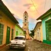 Oldtimer, bunte Kolonialhäuser & Kirchturm beim Sonnenuntergang in Trinidad auf Kuba - Gruppenreisen für Alleinreisende & Erlebnisreisen | QUERIDO MUNDO
